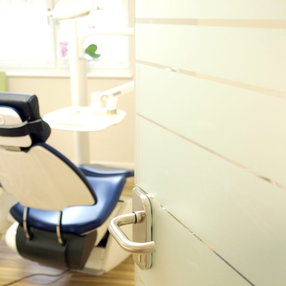 Praxis Zahnarztpraxis mit einem blauen Behandlungsstuhl und einer Tür im Vordergrund.